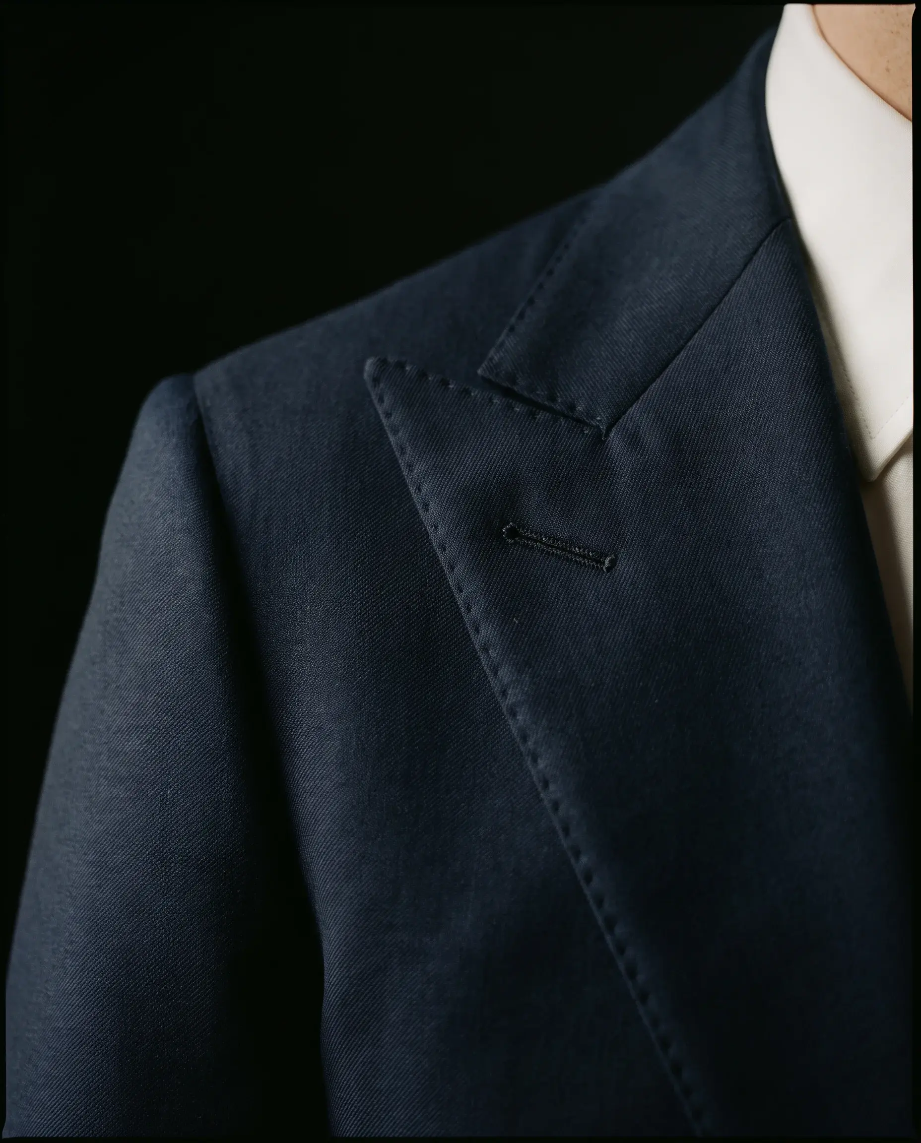 Close-up of the peak lapel on a navy jacket against a dark background