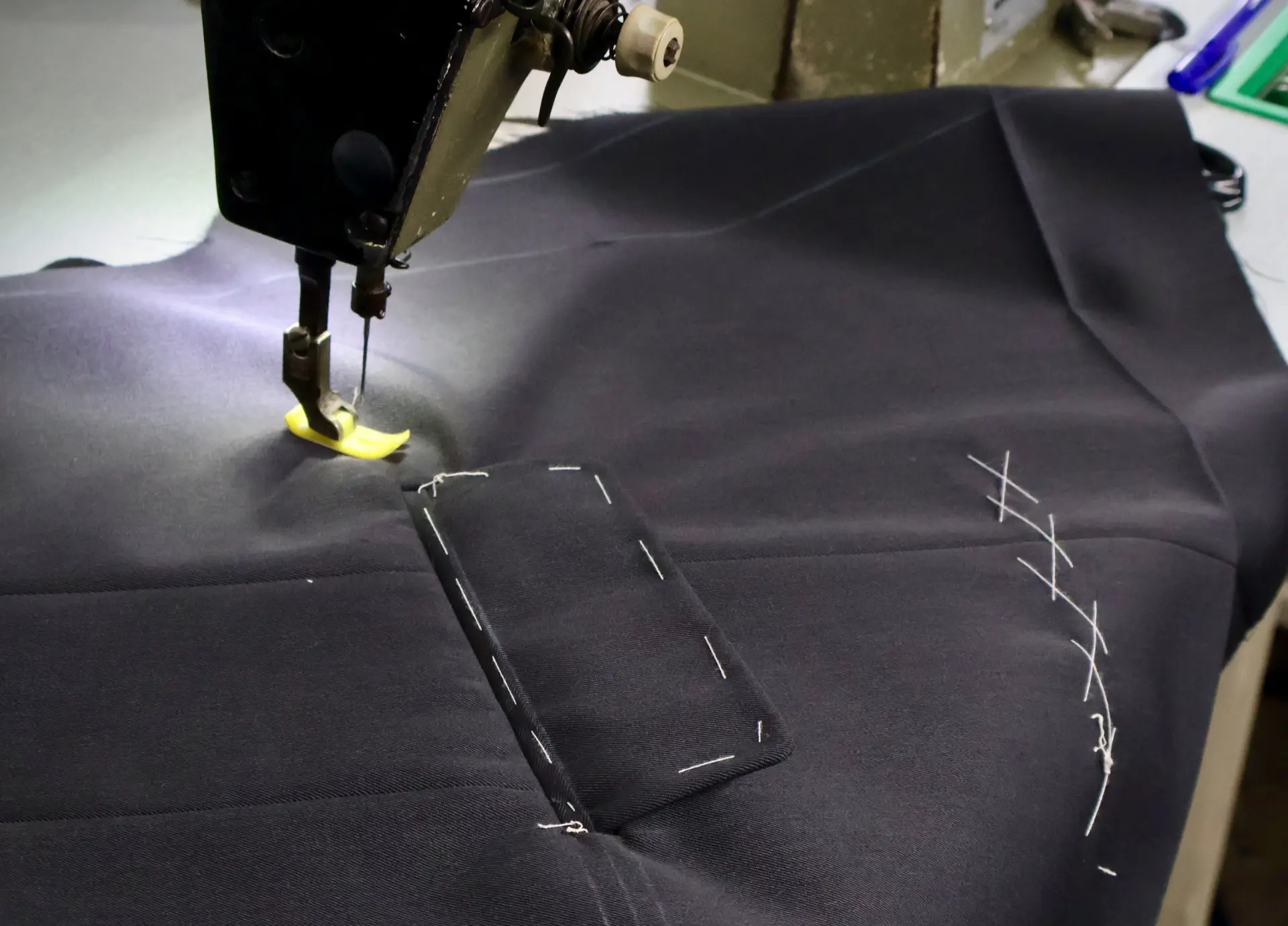 Sewing machine stitching dark suit cloth next to a pocket outline and basting stitches