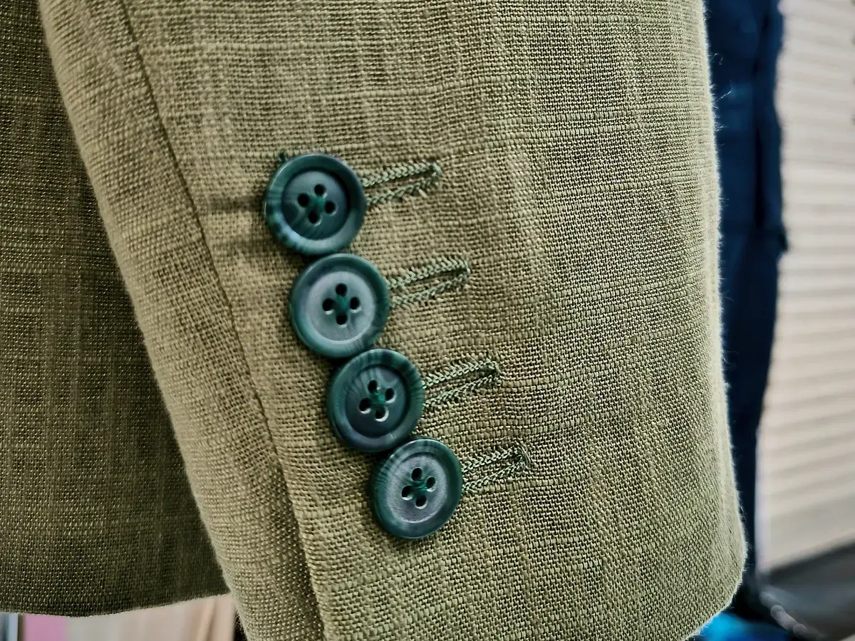 Sleeve of an olive linen bespoke jacket with four teal buttons on the cuff