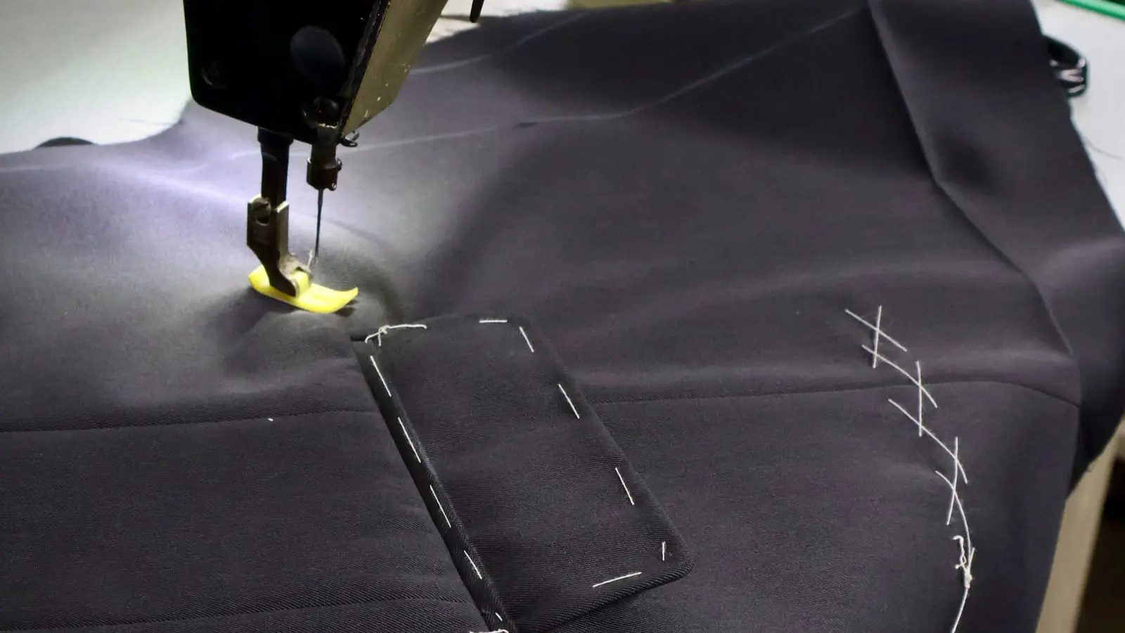 Sewing machine stitching a welt pocket on navy suit cloth with basting marks