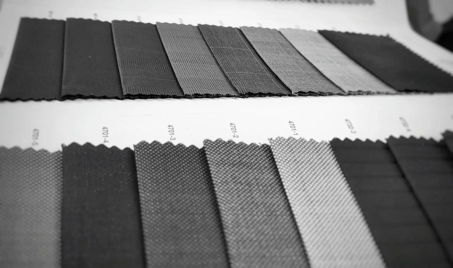 Black-and-white close-up of grey suiting swatches with pinstripes, checks and small textured weaves