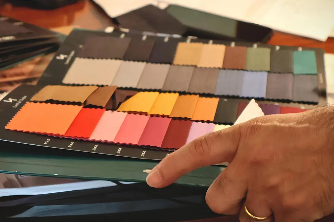 A hand pointing at a colourful fabric swatch book with orange, red, pink, yellow and grey samples
