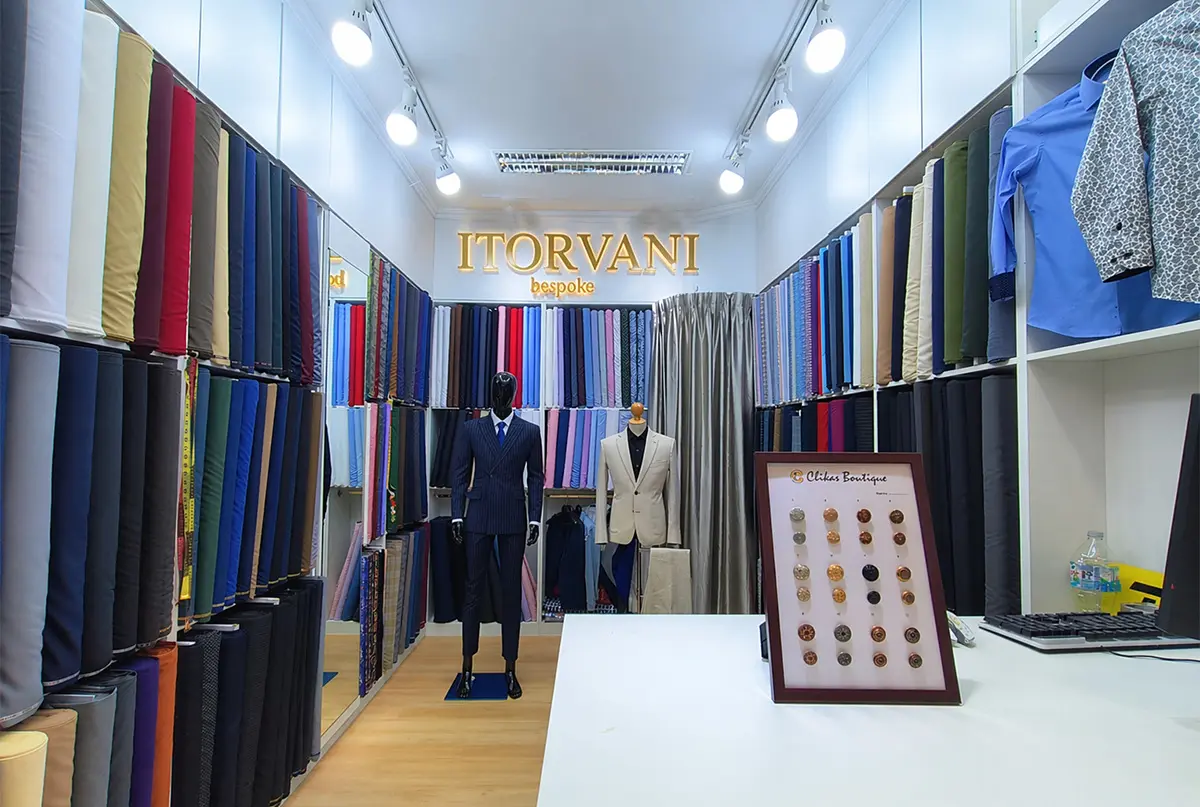 Inside the ITORVANI bespoke tailor shop at Platinum Fashion Mall, with fabric rolls, suit mannequins and the illuminated ITORVANI sign