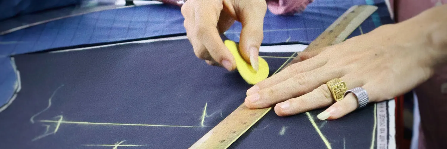 Tailor marking navy cloth with chalk and a wooden ruler before cutting