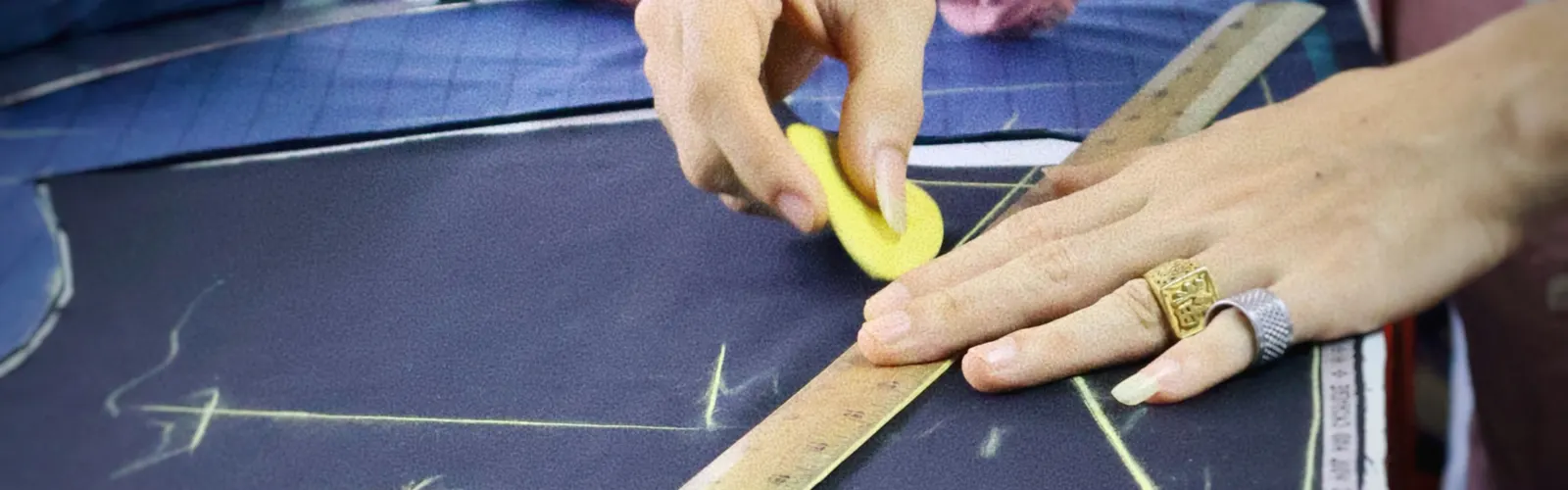 Tailor marking navy cloth with chalk and a wooden ruler before cutting