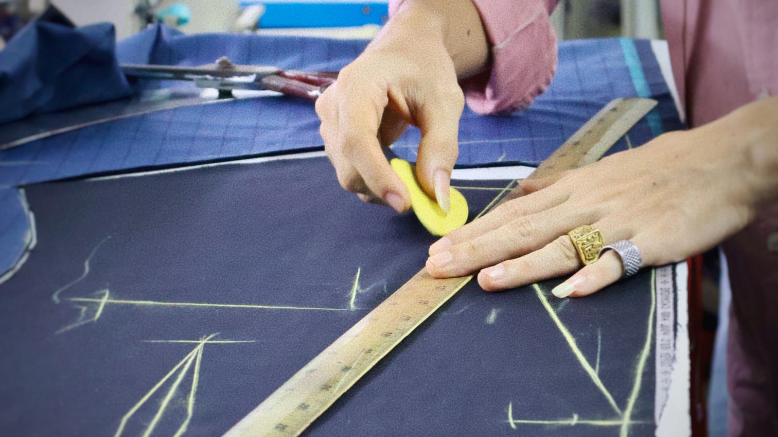 Tailor marking navy cloth with chalk and a wooden ruler before cutting