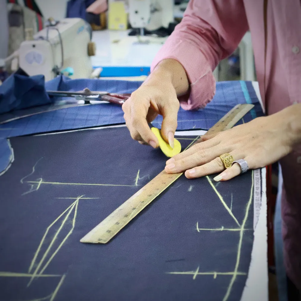 Tailor marking navy cloth with chalk and a wooden ruler before cutting