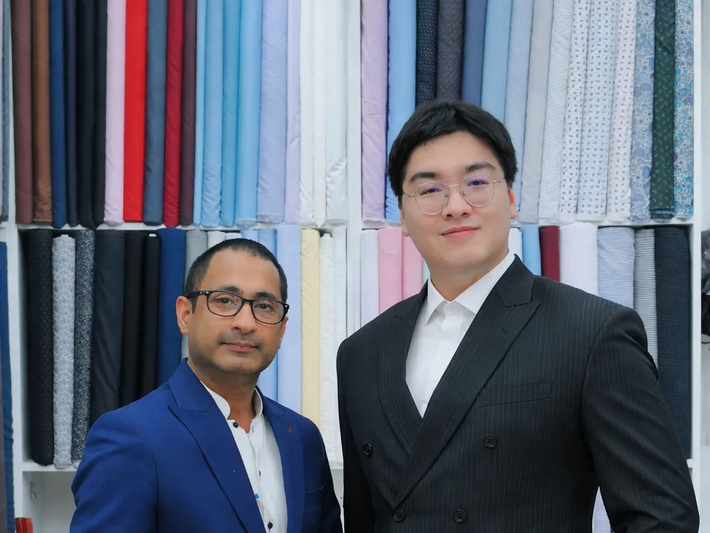Client in a black double-breasted suit standing beside a tailor in a blue jacket