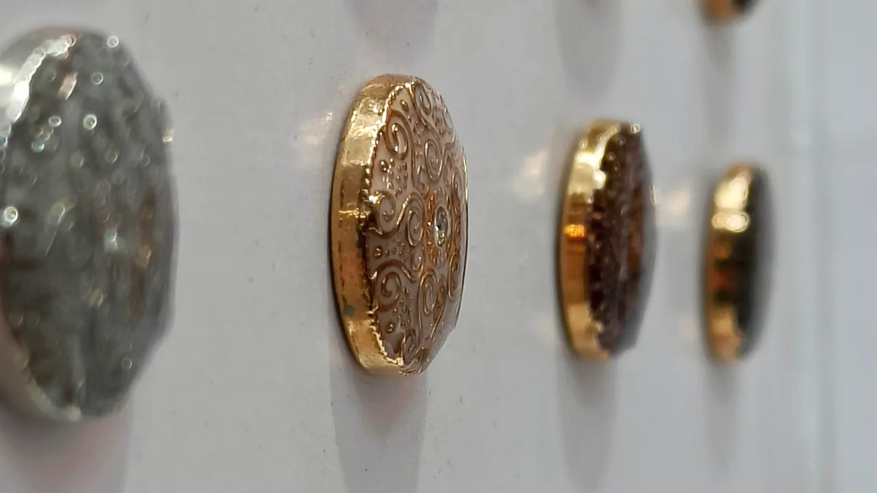 Engraved gold and silver metal suit buttons lined up on a display