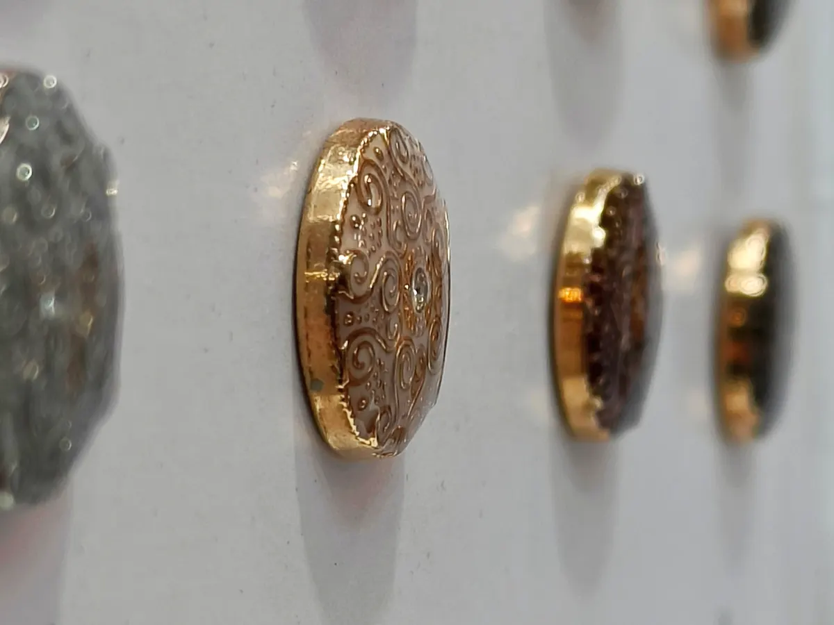 Engraved gold and silver metal suit buttons lined up on a display