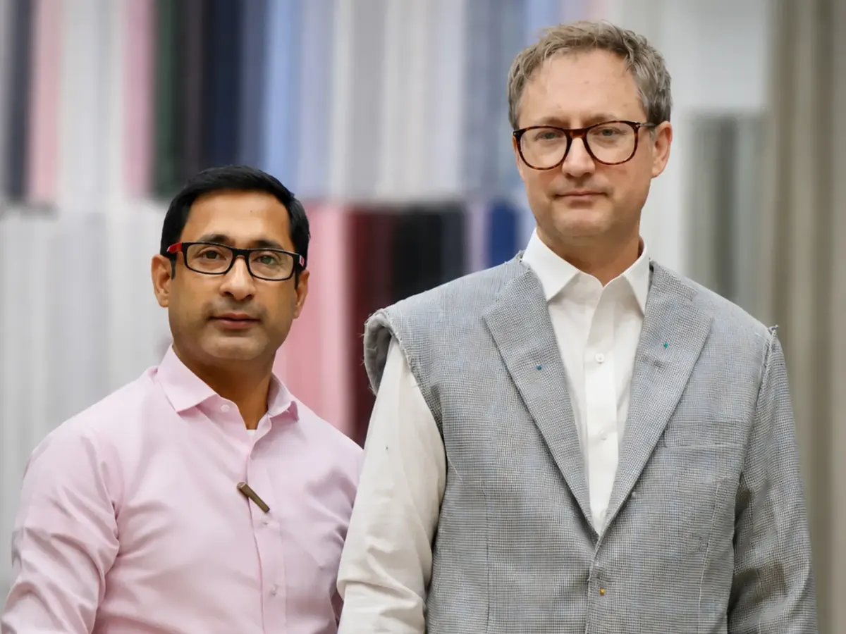 Client in a grey checked waistcoat-style jacket beside a tailor in a pink shirt