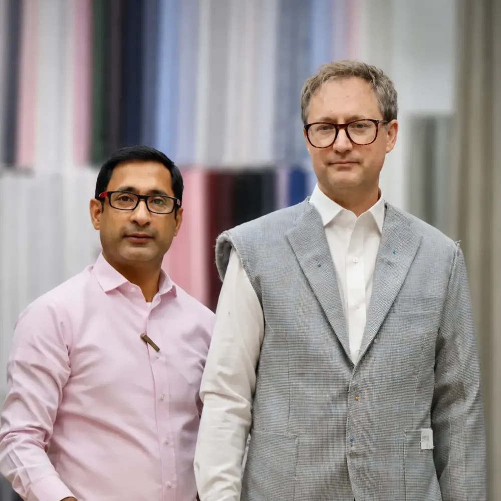 Client in a grey checked waistcoat-style jacket beside a tailor in a pink shirt
