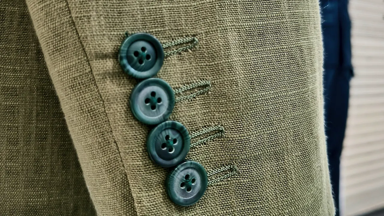 Sleeve of an olive linen bespoke jacket with four teal buttons on the cuff