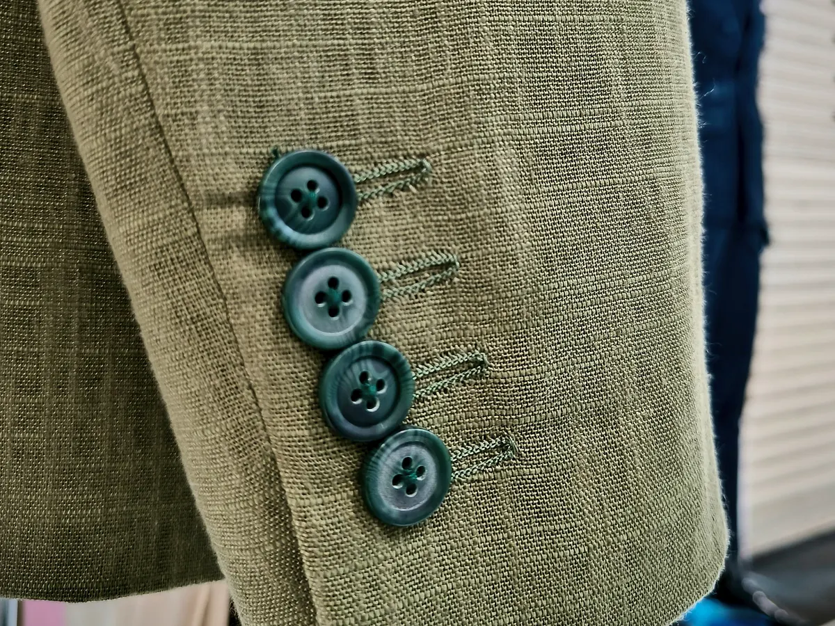Sleeve of an olive linen bespoke jacket with four teal buttons on the cuff