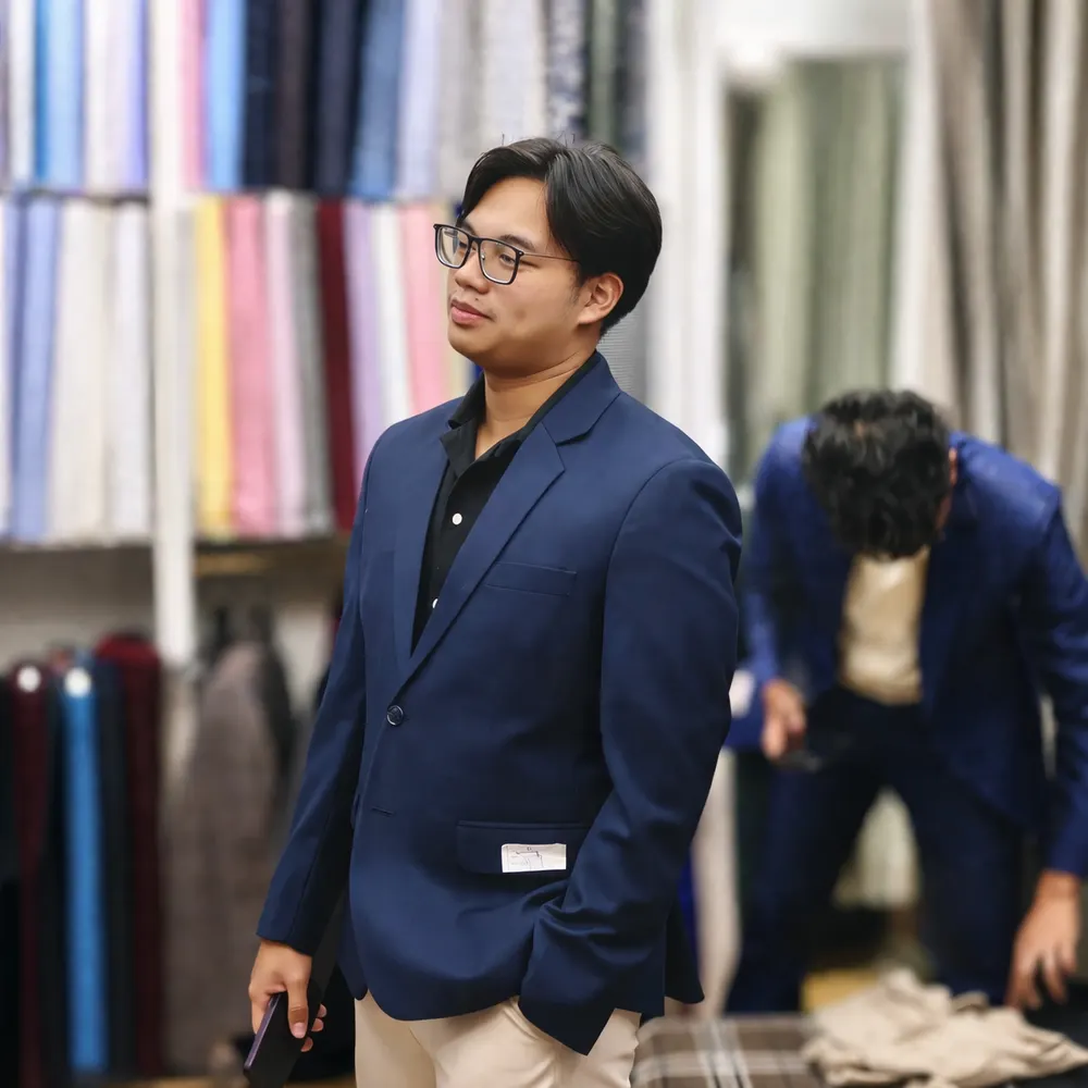 Man in a tailored navy blazer standing beside rolls of fabric