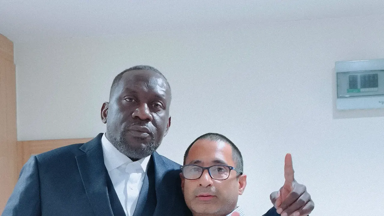 Client in a navy three-piece suit posing with a tailor after a fitting