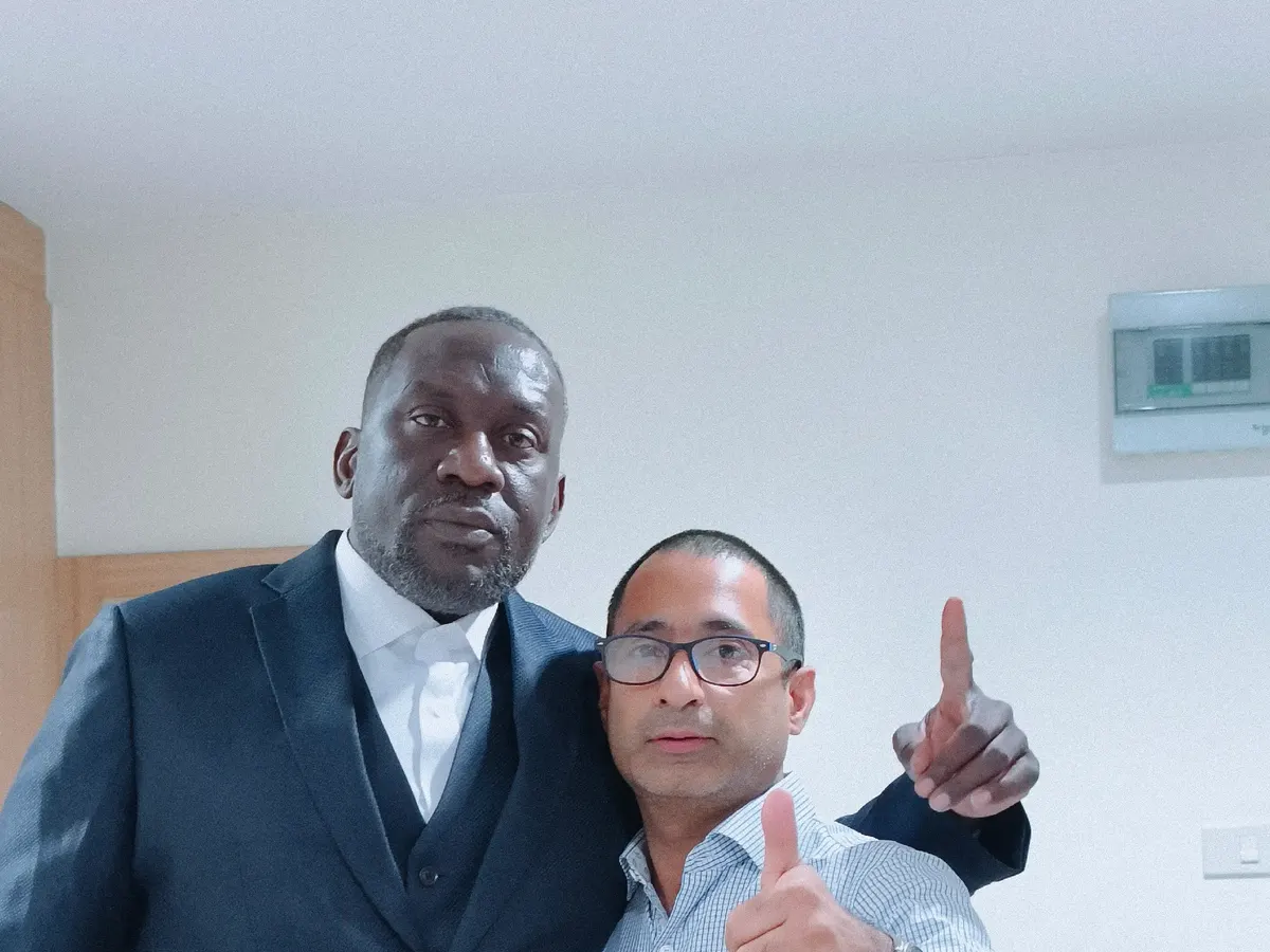 Client in a navy three-piece suit posing with a tailor after a fitting
