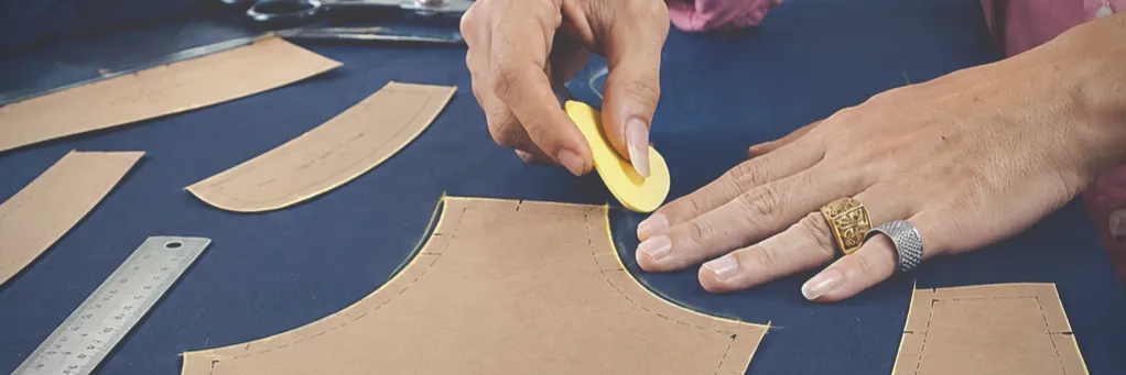 Tailor chalking around paper pattern pieces laid on navy suit cloth