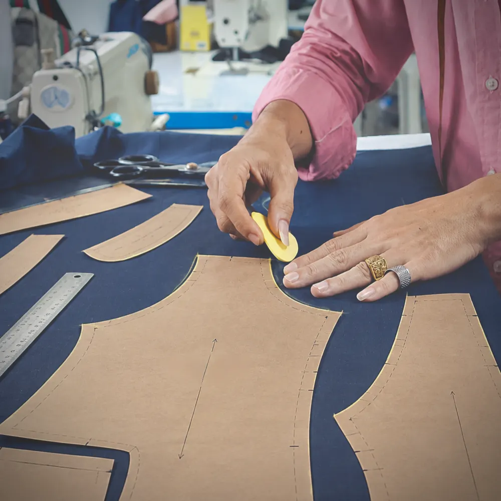 Tailor chalking around paper pattern pieces laid on navy suit cloth