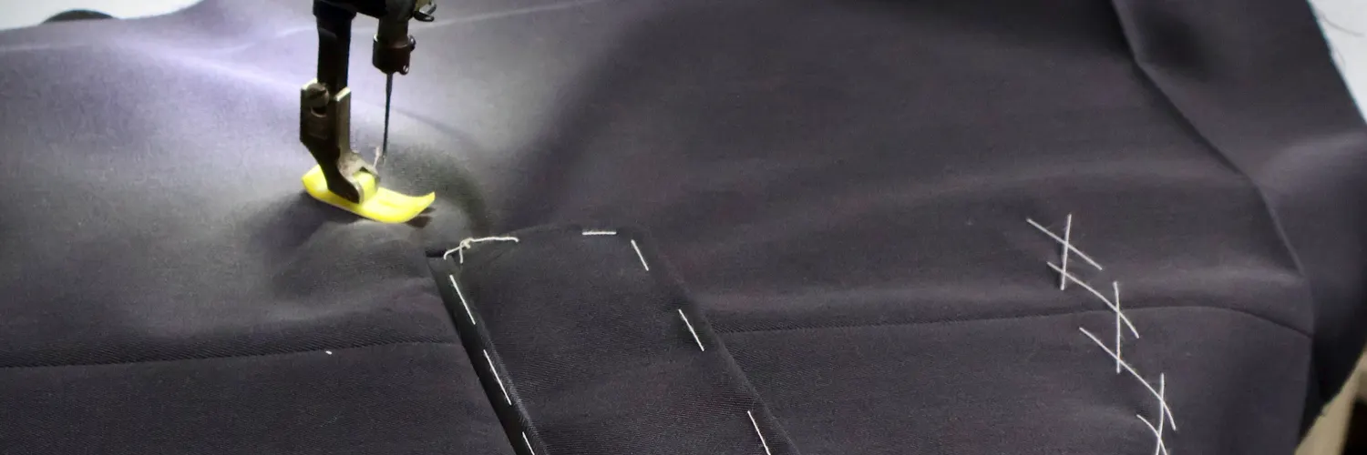 Sewing machine stitching a welt pocket on navy suit cloth with basting marks