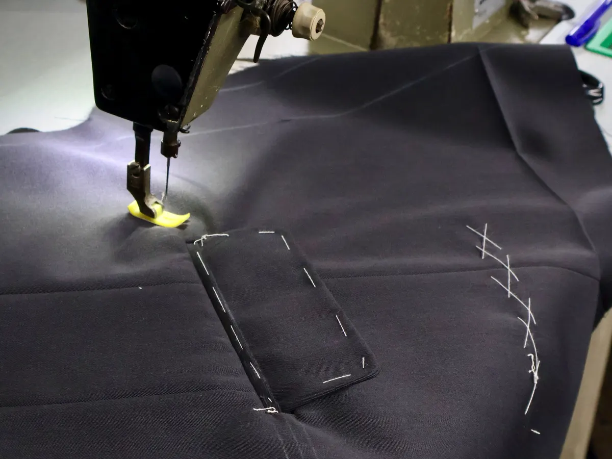 Sewing machine stitching a welt pocket on navy suit cloth with basting marks