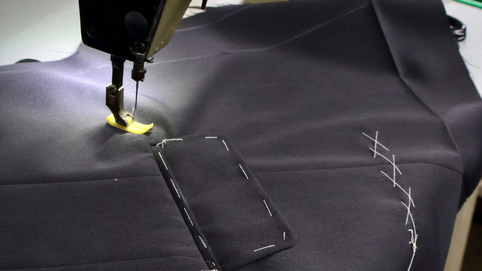 Sewing machine stitching a welt pocket on navy suit cloth with basting marks