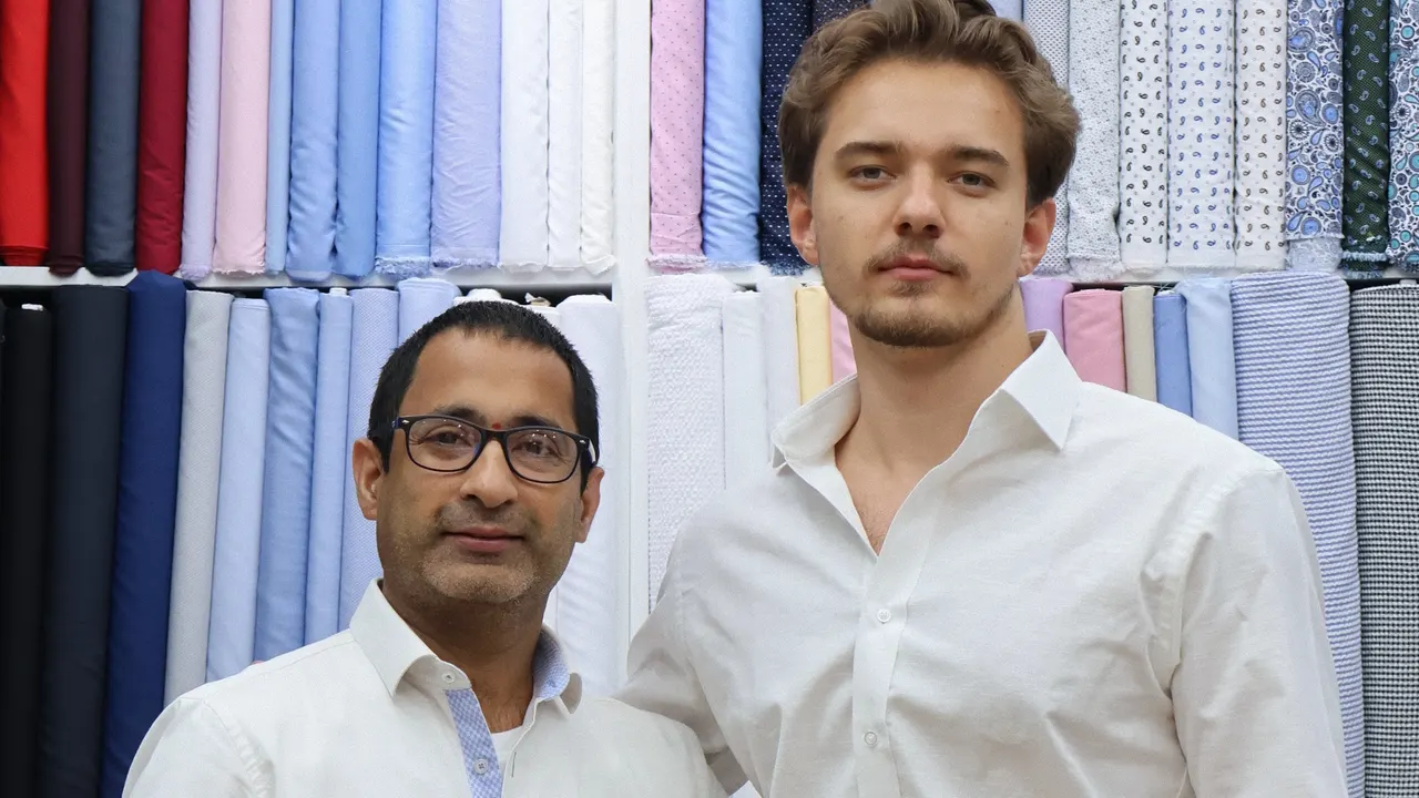 Two men in tailored white dress shirts standing in front of shirt fabrics