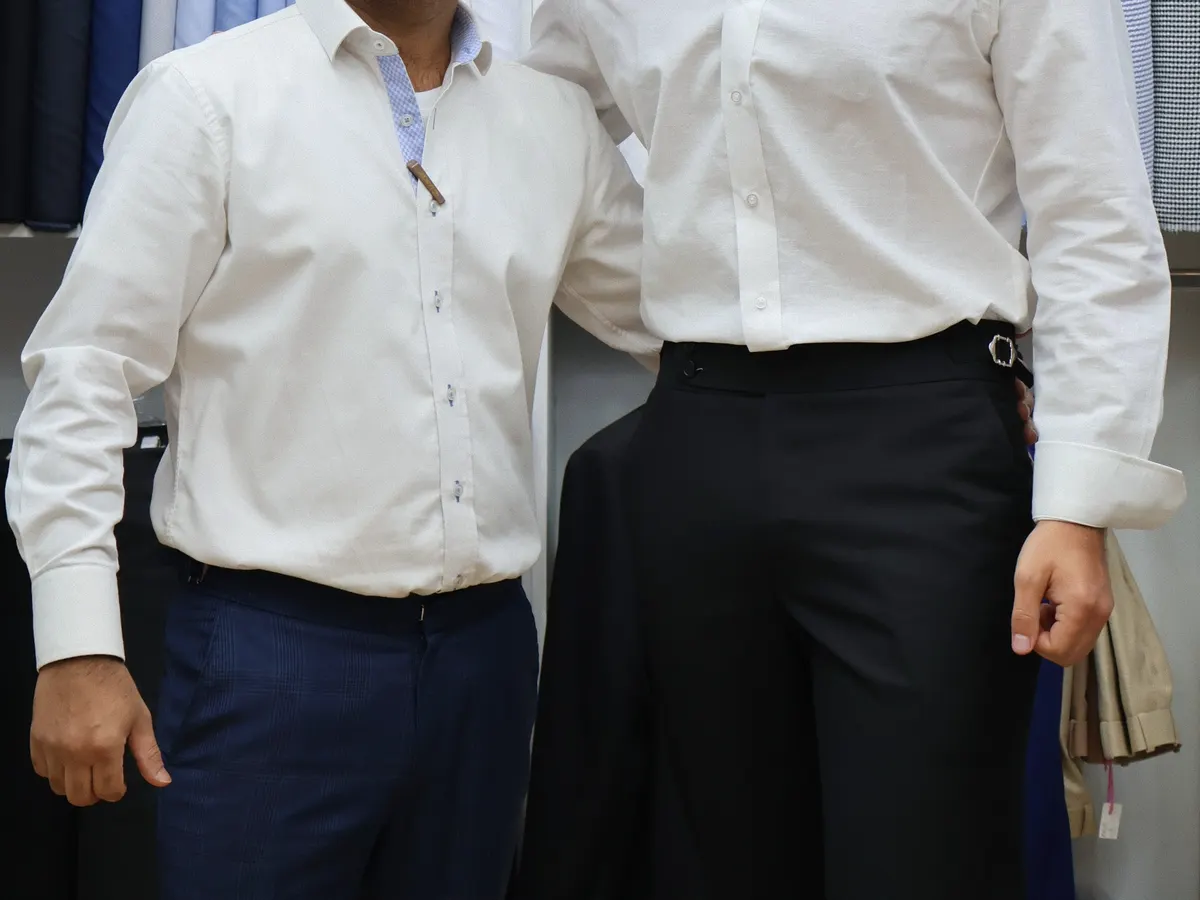 Two men in tailored white dress shirts standing in front of shirt fabrics