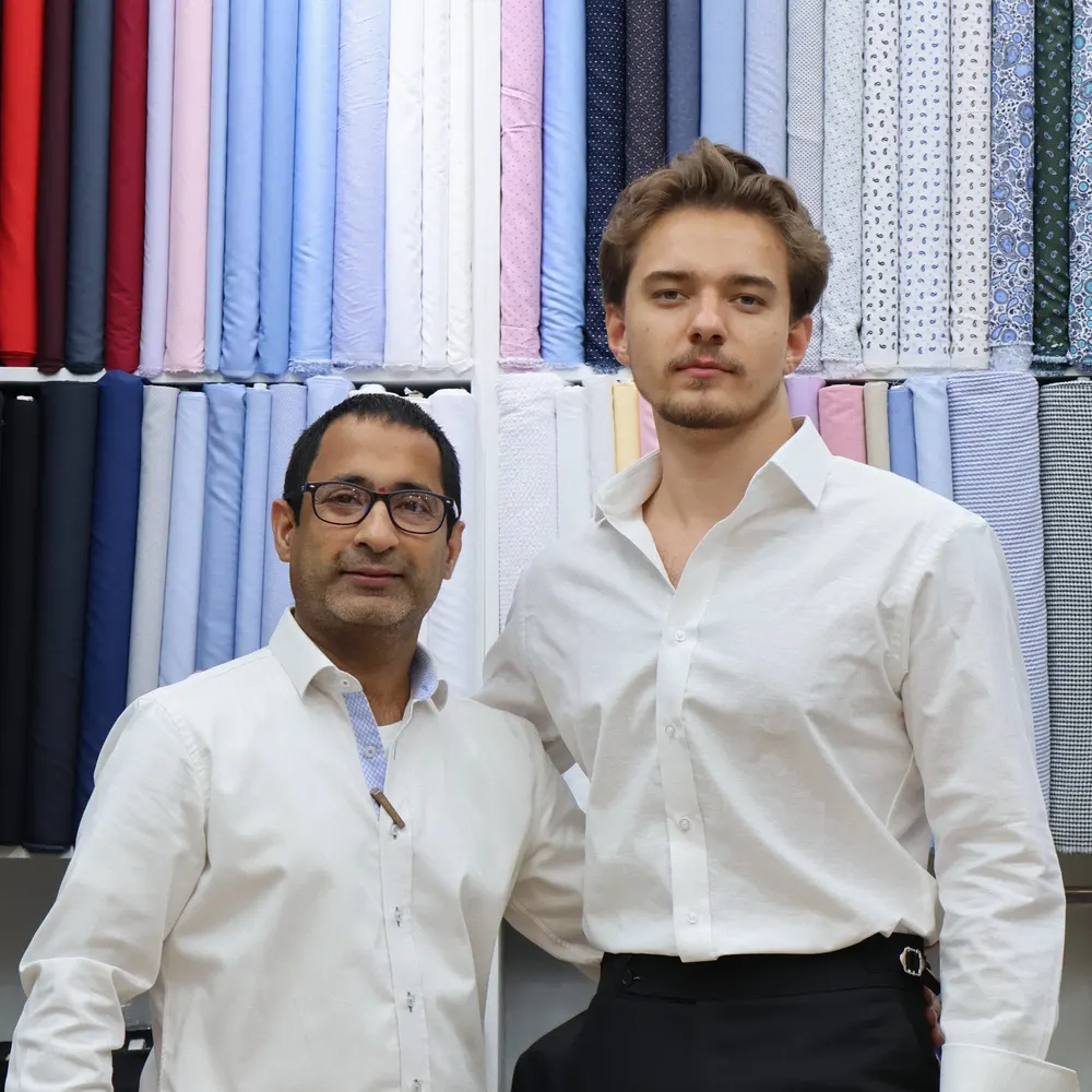 Two men in tailored white dress shirts standing in front of shirt fabrics