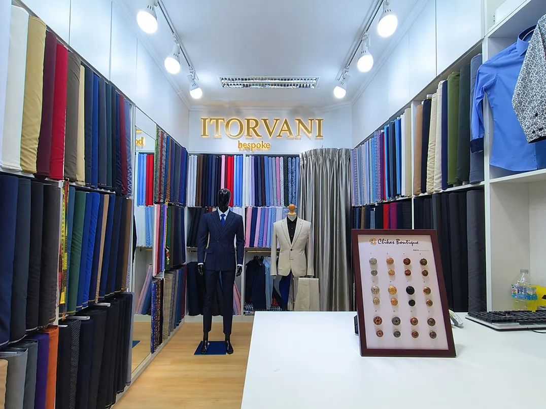 Inside the ITORVANI bespoke tailor shop at Platinum Fashion Mall, with fabric rolls, suit mannequins and the illuminated ITORVANI sign