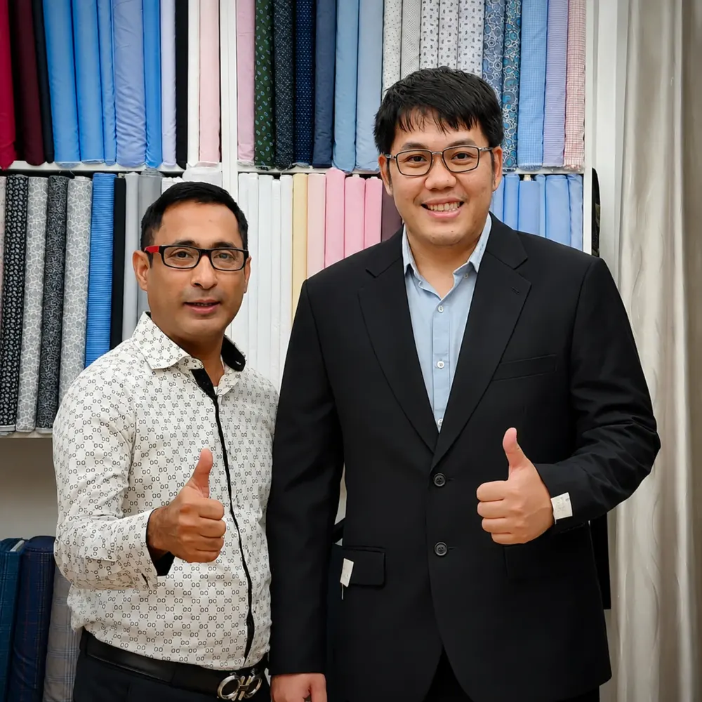 Tailor and a client in a black suit jacket smiling in front of the fabric wall