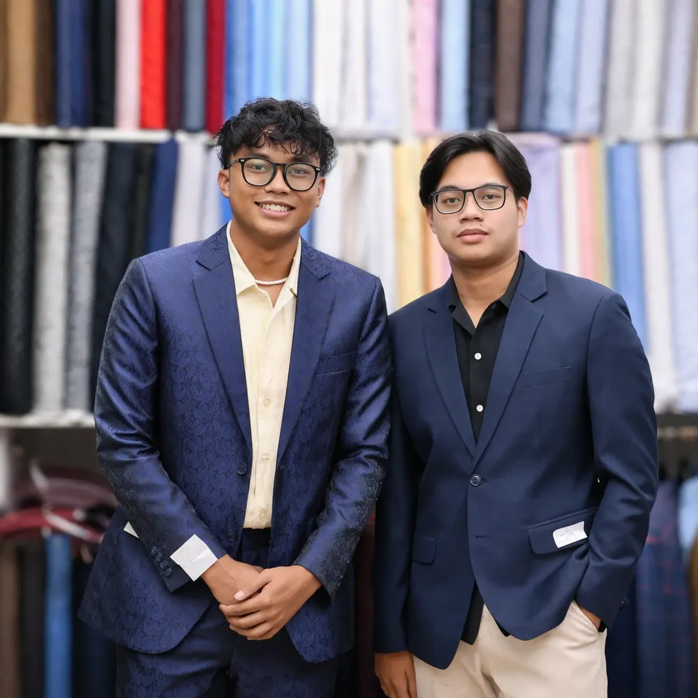 Two young men in navy tailored blazers standing in front of the fabric wall