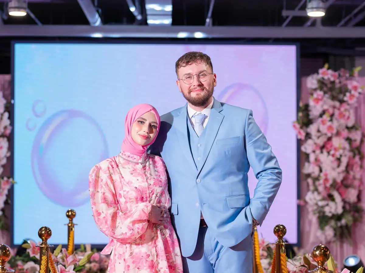 Groom in a light blue three-piece suit standing beside his bride on a flower-lined stage