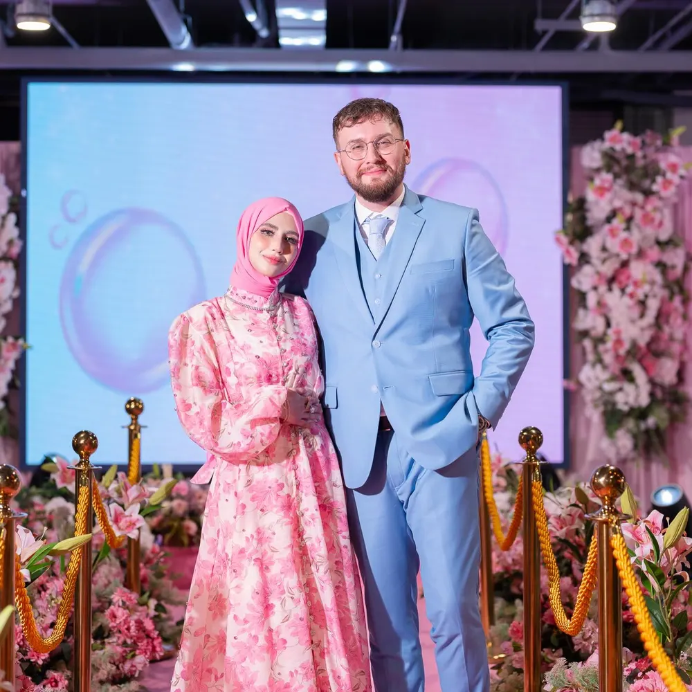 Groom in a light blue three-piece suit standing beside his bride on a flower-lined stage