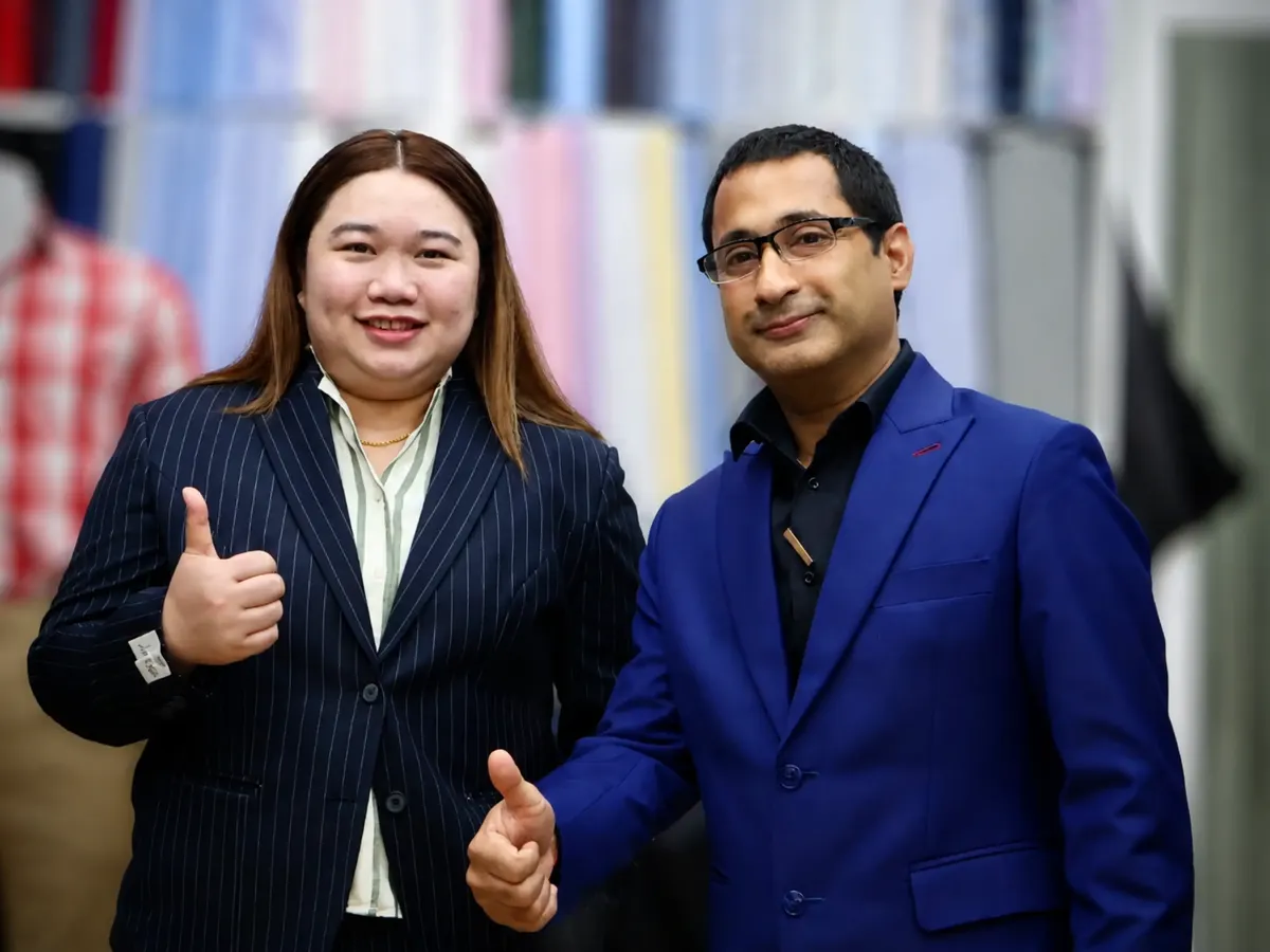 Woman in a navy pinstripe blazer and a tailor in a blue jacket both giving a thumbs up