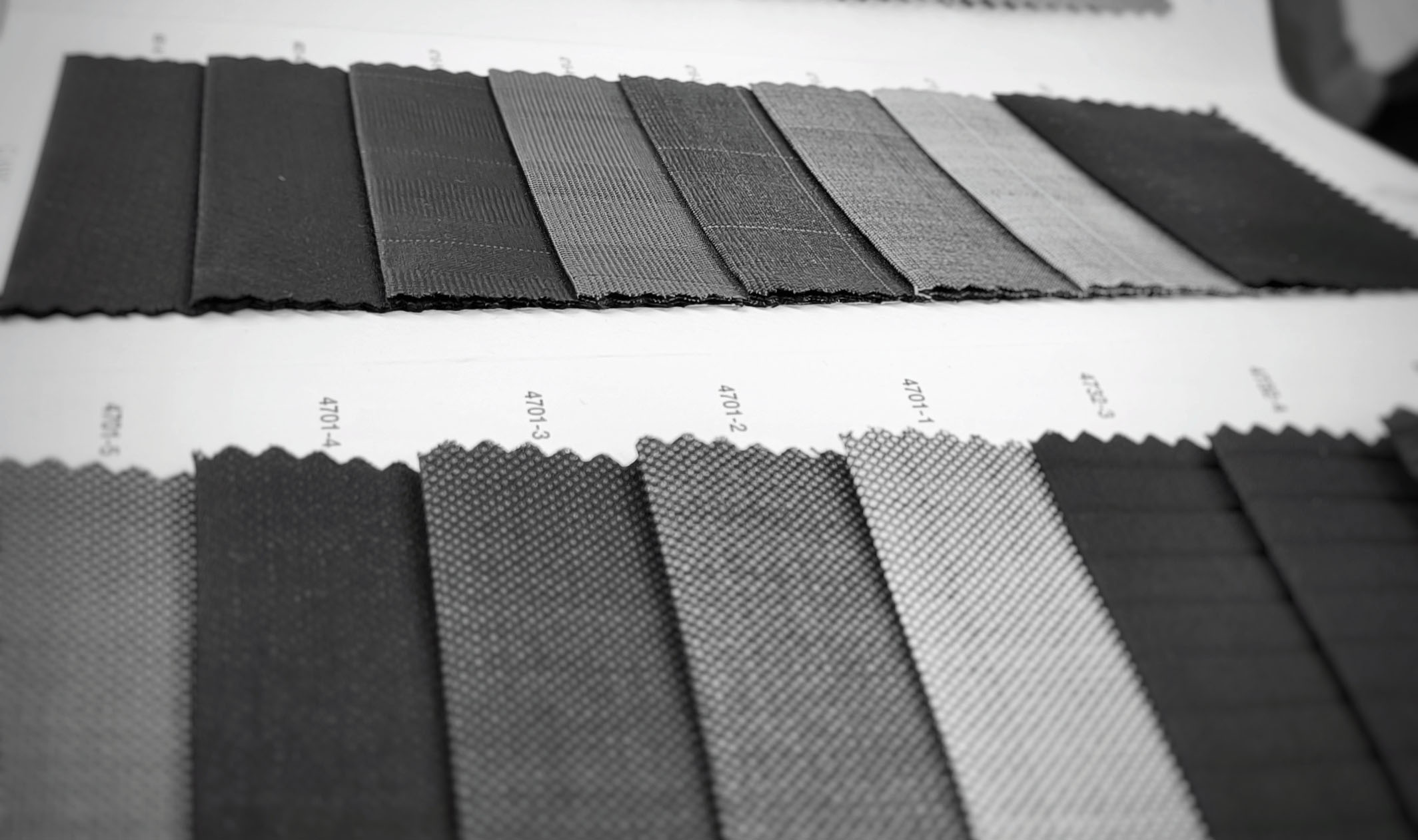 Black-and-white close-up of grey suiting swatches with pinstripes, checks and small textured weaves